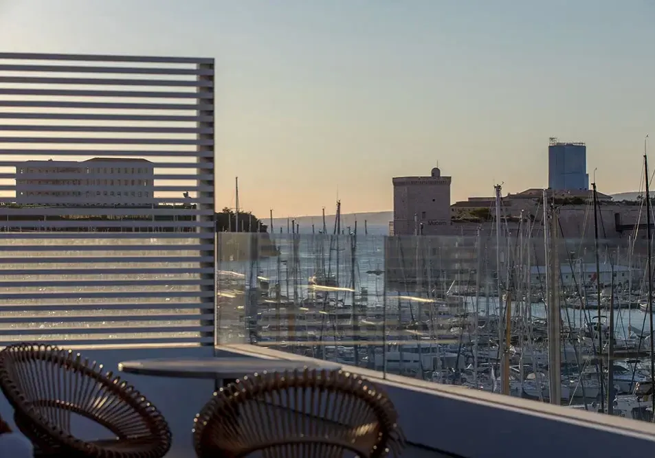 Terrasse d'un espace de coworking marseillais avec vue panoramique sur le Vieux-Port et le fort Saint-Jean au coucher du soleil.
