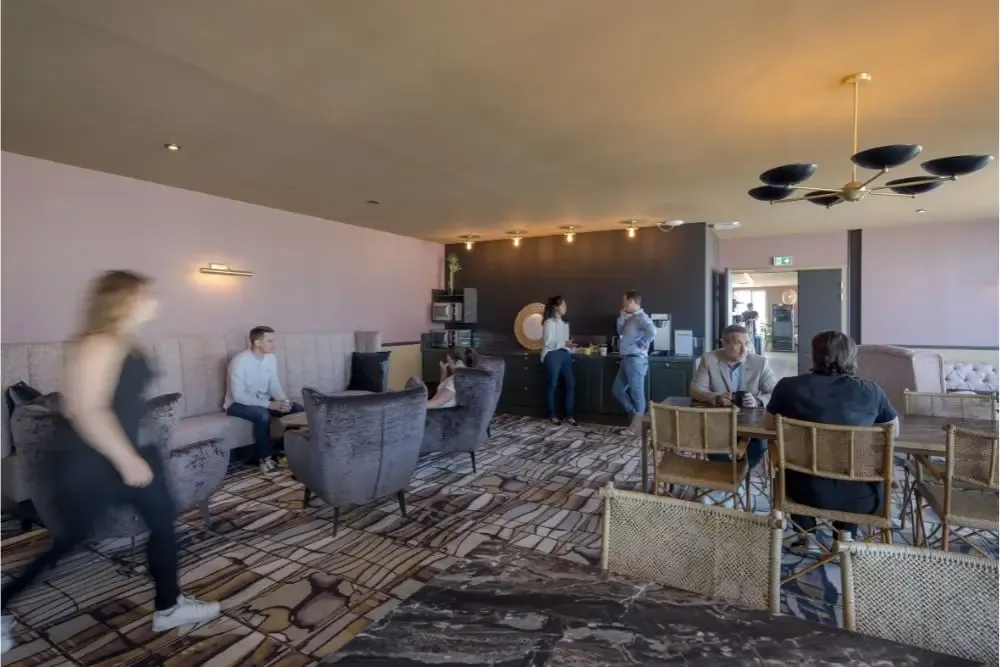 Zone de détente élégante dans un espace de coworking à Nantes avec fauteuils confortables, professionnels en discussion et coin café.