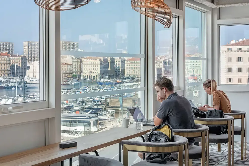 Espace de travail avec bureaux face aux baies vitrées offrant une vue spectaculaire sur le Vieux-Port et les bateaux de Marseille.