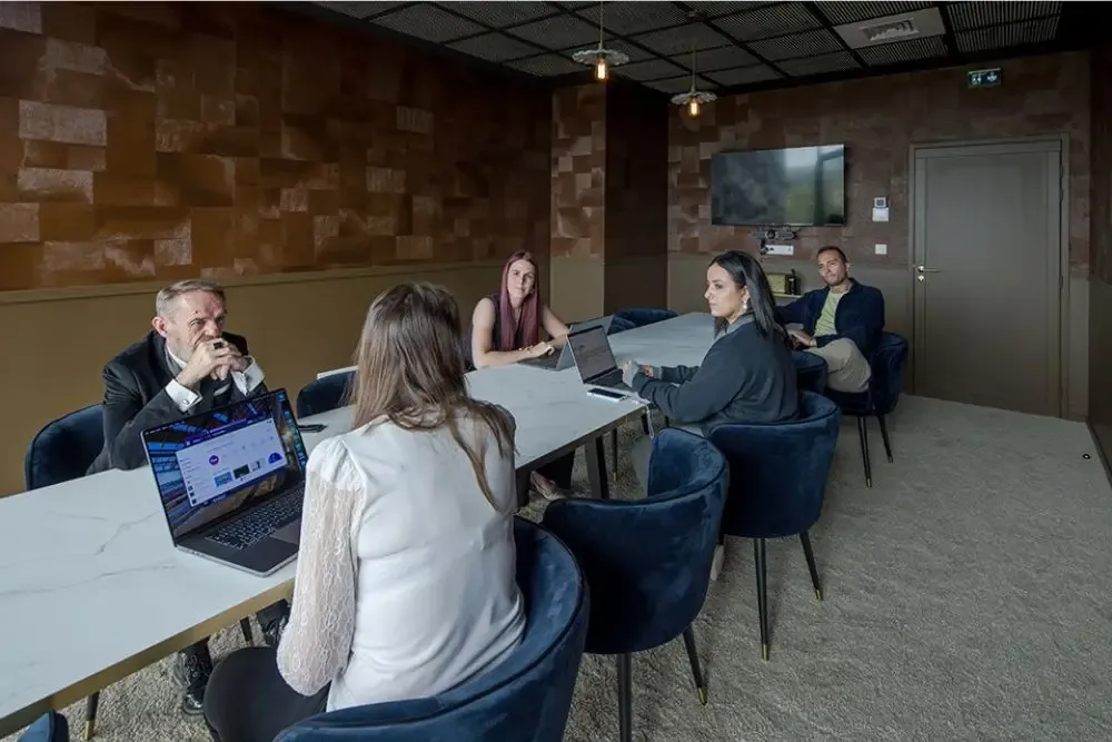 Salle de réunion élégante à Now coworking Metz avec cinq professionnels travaillant autour d'une table en marbre, écrans d'ordinateurs ouverts et décor design.