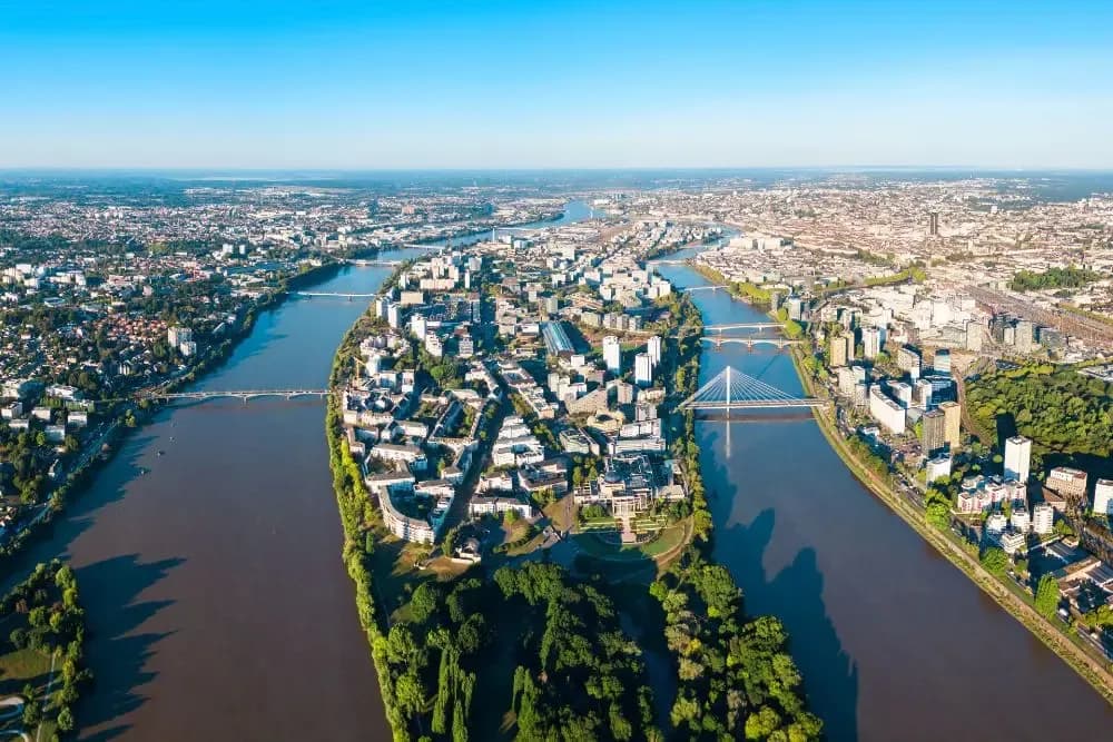 Panorama aérien de l'Île de Nantes entourée par la Loire, zone stratégique pour la location de bureaux avec ponts et espaces verts.