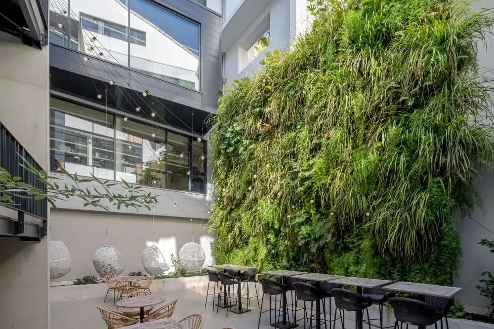 Patio moderne avec impressionnant mur végétal, fauteuils suspendus et espaces de convivialité, favorisant la détente et le bien-être au travail.