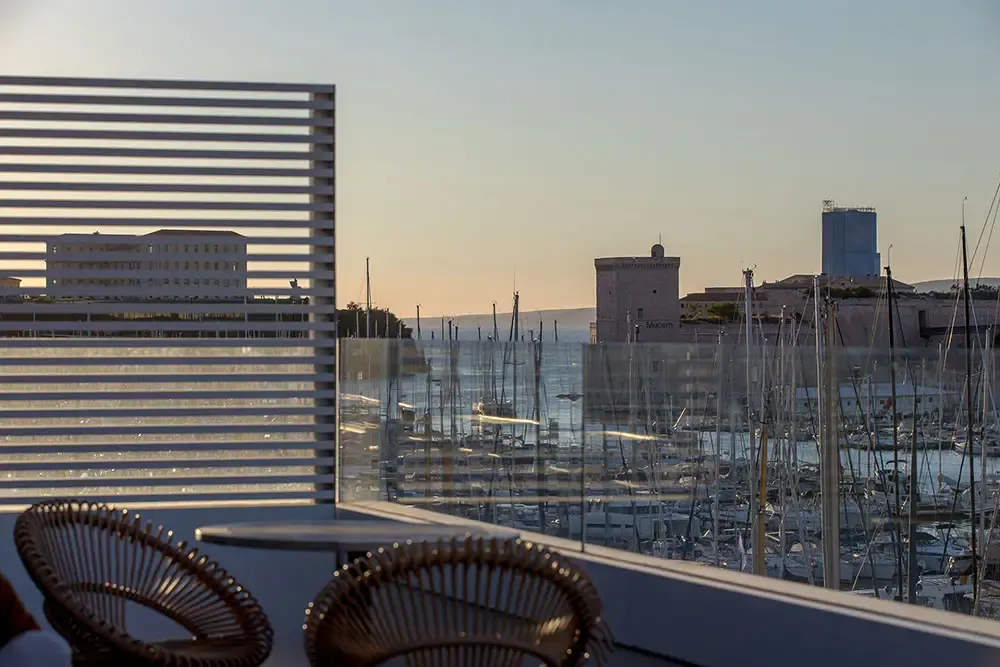 Terrasse d'un espace de coworking marseillais avec vue panoramique sur le Vieux-Port et le fort Saint-Jean au coucher du soleil.