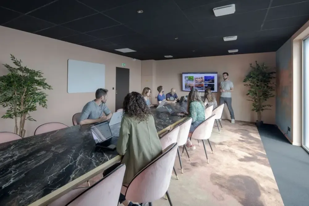 Grande salle de réunion dans un espace de coworking nantais avec professionnels assistant à une présentation sur écran et table en marbre noir.