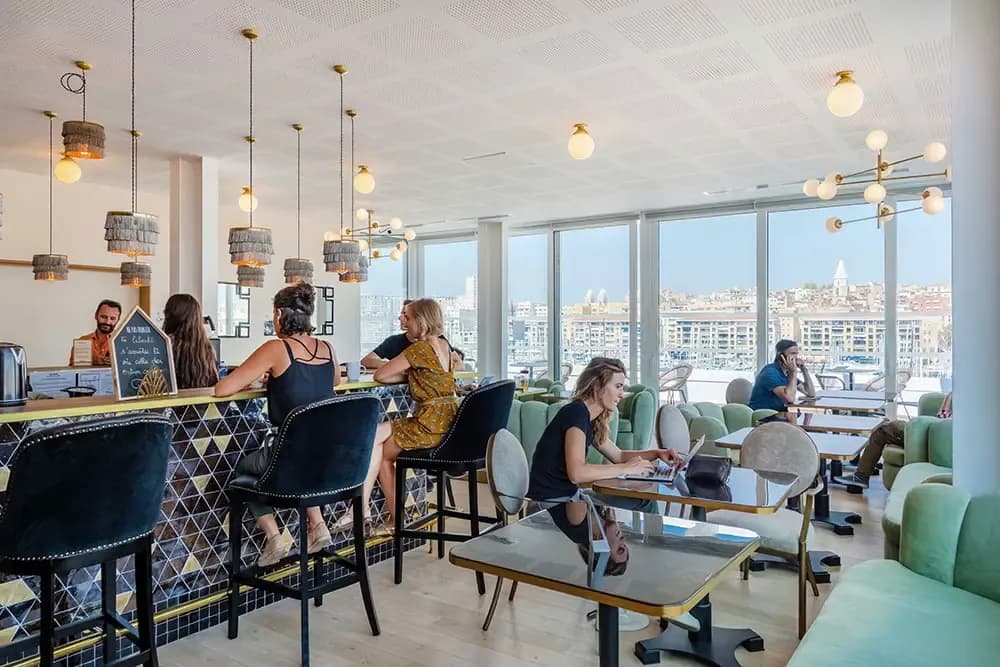 Bar élégant d'un espace de coworking marseillais offrant une vue panoramique sur le Vieux-Port où professionnels travaillent et échangent.