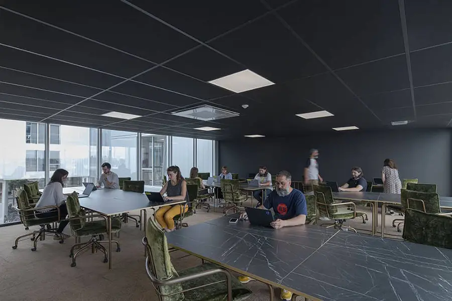 Un large bureau privatif à Nantes avec des tables en marbre noir et des chaises en velours vert, dans un espace lumineux avec des professionnels concentrés, chacun engagé dans son travail, offrant une atmosphère productive et sereine.