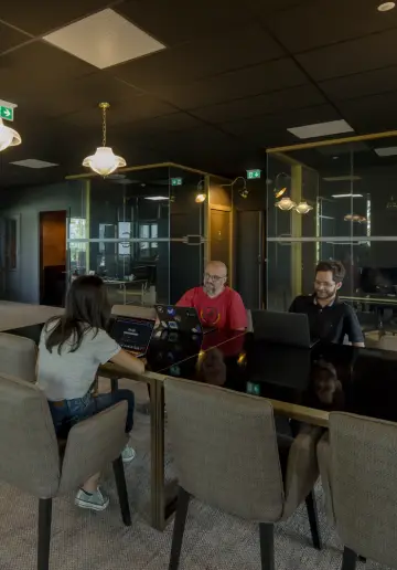 Trois coworkers travaillant ensemble dans une salle moderne avec un éclairage chaleureux.