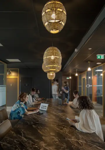 Coworkers travaillant ensemble dans une salle avec une table en marbre et des suspensions lumineuses modernes.