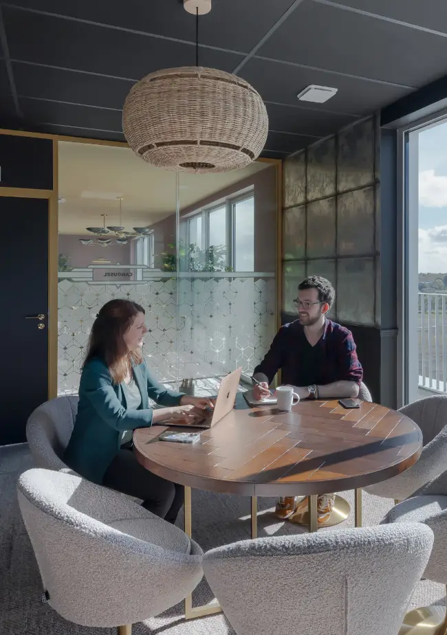 Deux coworkers collaborant autour d’une table ronde en bois dans une salle lumineuse à Nantes.