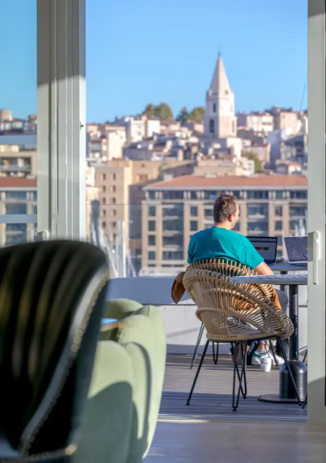 Terrasse ensoleillée avec vue sur la ville et coworker en train de travailler à Now coworking Marseille.